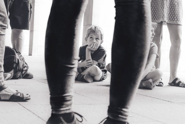 grayscale photography of boy sitting on the floor watching the person in front of him