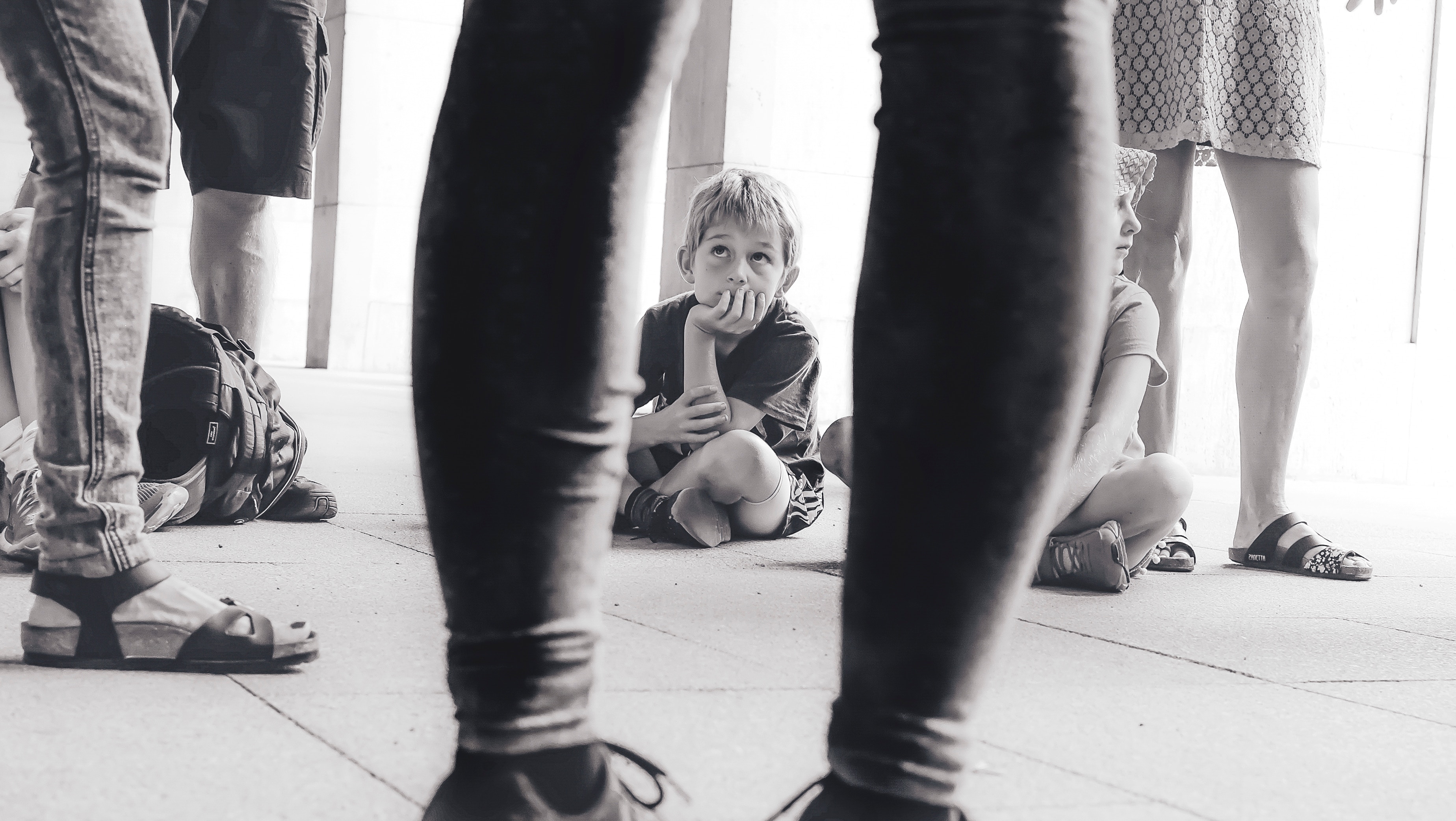 grayscale photography of boy sitting on the floor watching the person in front of him